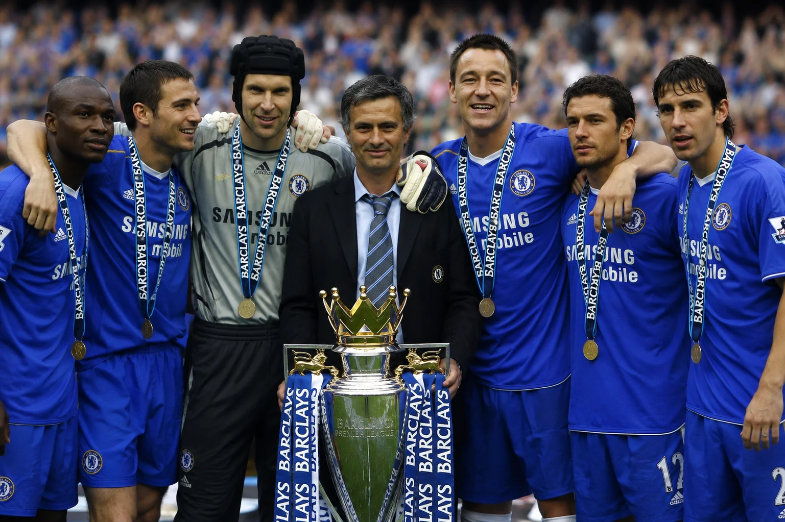 Manager José Mourinho posed with Chelsea players Claude Makélélé, Frank Lampard, Petr Čech, John Terry, Wayne Bridge, and Paulo Ferreira gathered around the Premier League trophy, with each player wearing their winner's medal following the 2004–05 championship season.