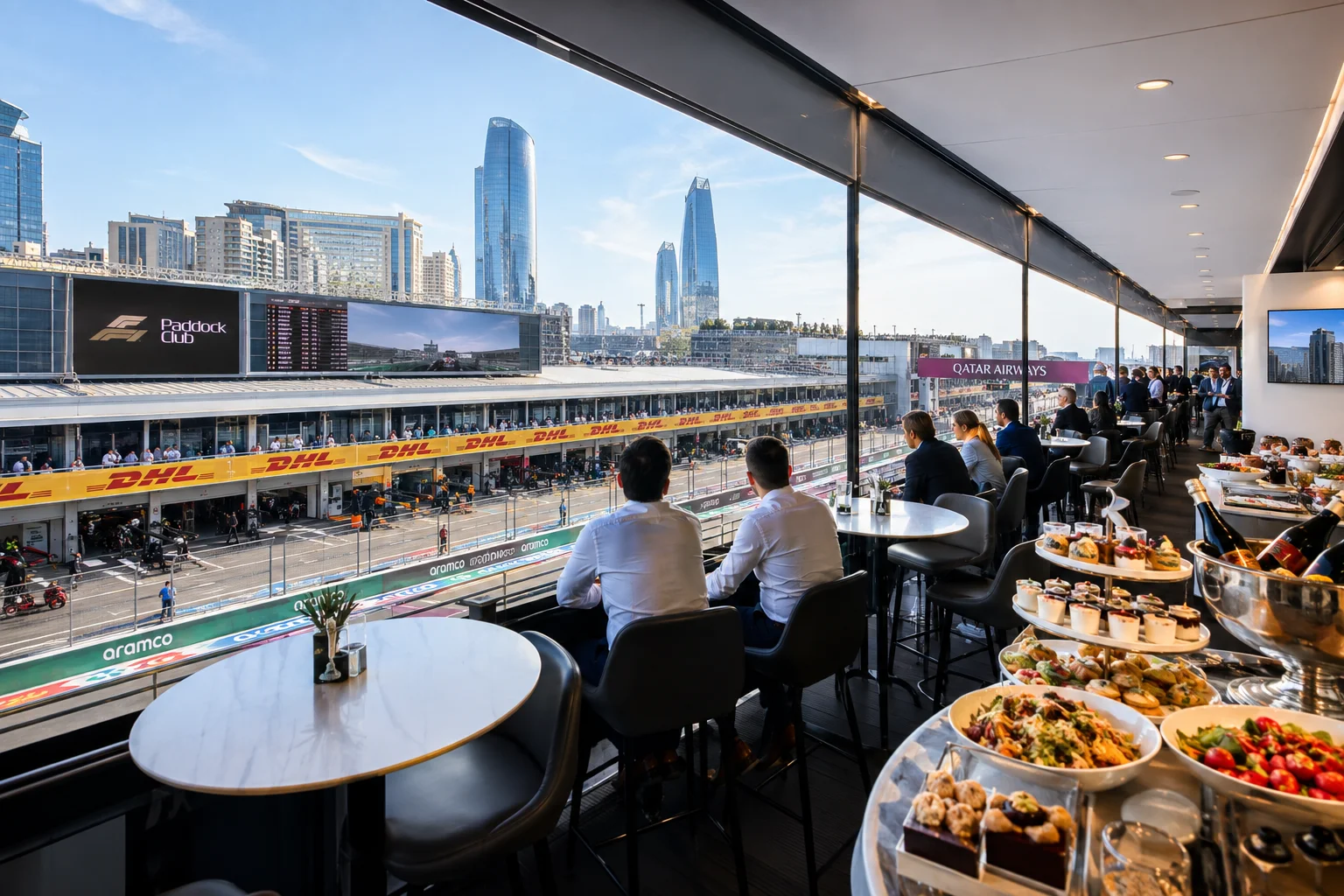 Guests dining in an indoor high-end Paddock Club balcony suite overlooking the Baku Grand Prix main straight and pit garages.