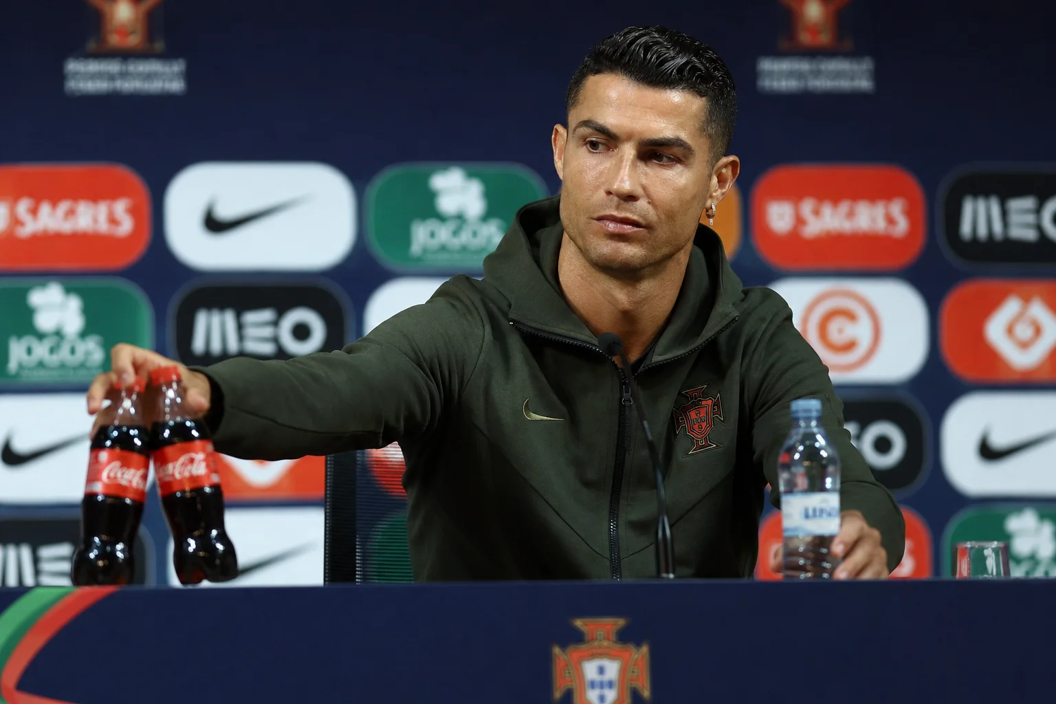 A viral media infographic recreating Cristiano Ronaldo's famous press conference moment during the UEFA Euro 2020 tournament. On the left, Ronaldo is pictured sitting behind a press table, actively moving two bottles of Coca-Cola out of the camera frame while holding up a bottle of water instead. The right side features a bold headline and a graphical timeline mapping the massive global social media impact and immediate multi-billion-dollar stock market valuation dip that followed his "Agua" gesture.