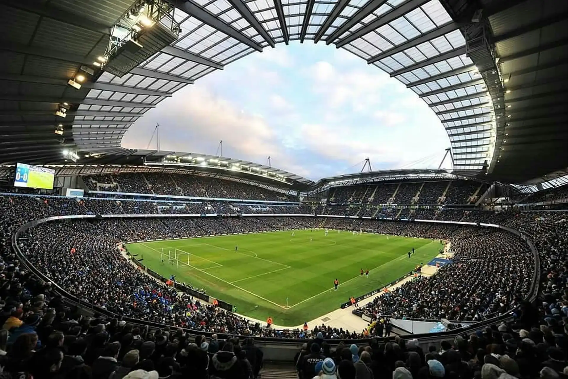 Panoramic matchday view inside Etihad Stadium with a packed crowd, open roof and football pitch during a Manchester City game