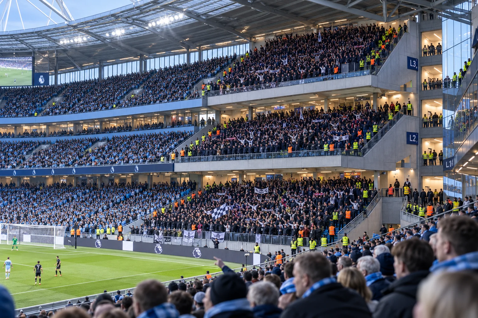 A crowded multi-tier stand at Etihad Stadium filled with fans, showing levels labeled L1, L2, and L3 on the concrete pillars, viewed from adjacent seats looking across the pitch.
