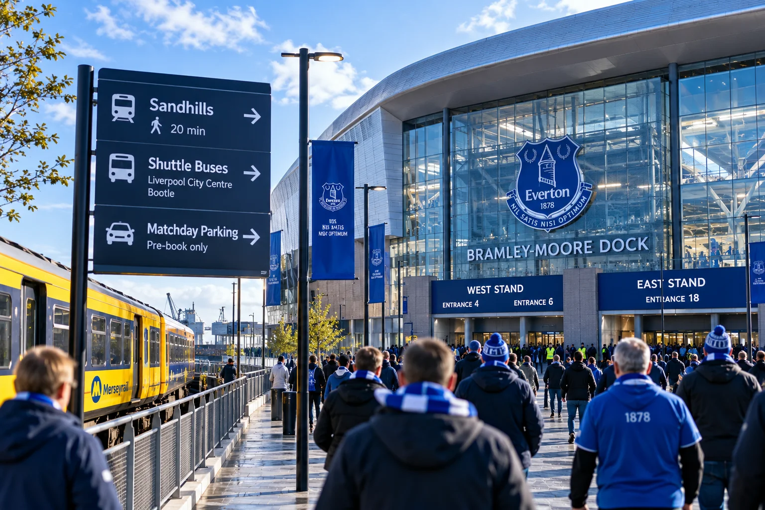 مشجعو كرة القدم يسيرون نحو مدخل ملعب براملي-مور دوك بجوار لافتات النقل الاتجاهية وقطار Merseyrail في يوم المباراة.