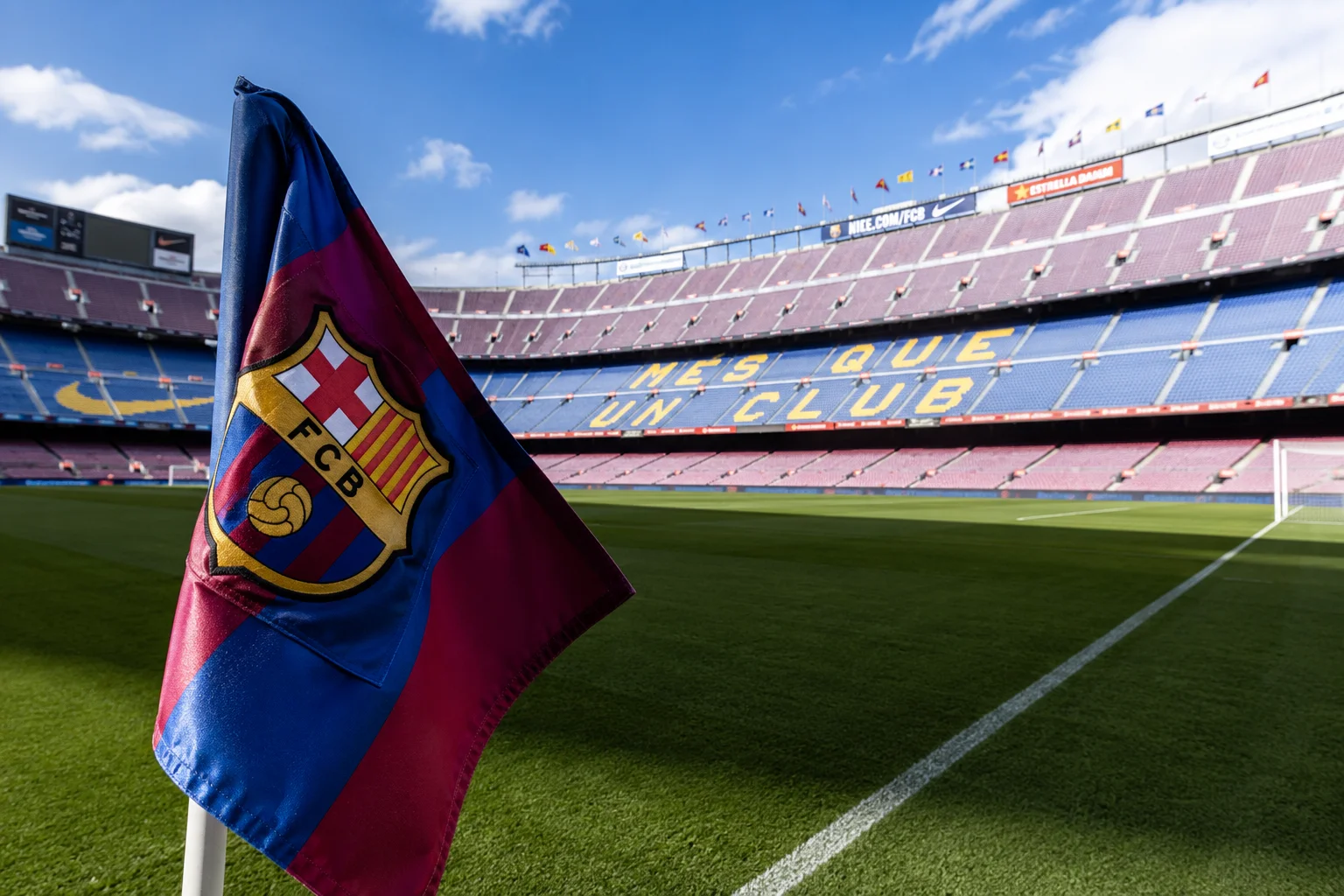 عرض قريبة لعلمة ركن تعرض شعار FC برشلونة الواقف على الملعب في كامب نو، مع الشعار الشهير مِسْ كَي ن كلُم مرئي باللون الأصفر على المقاعد الزرقاء في الخلفية.