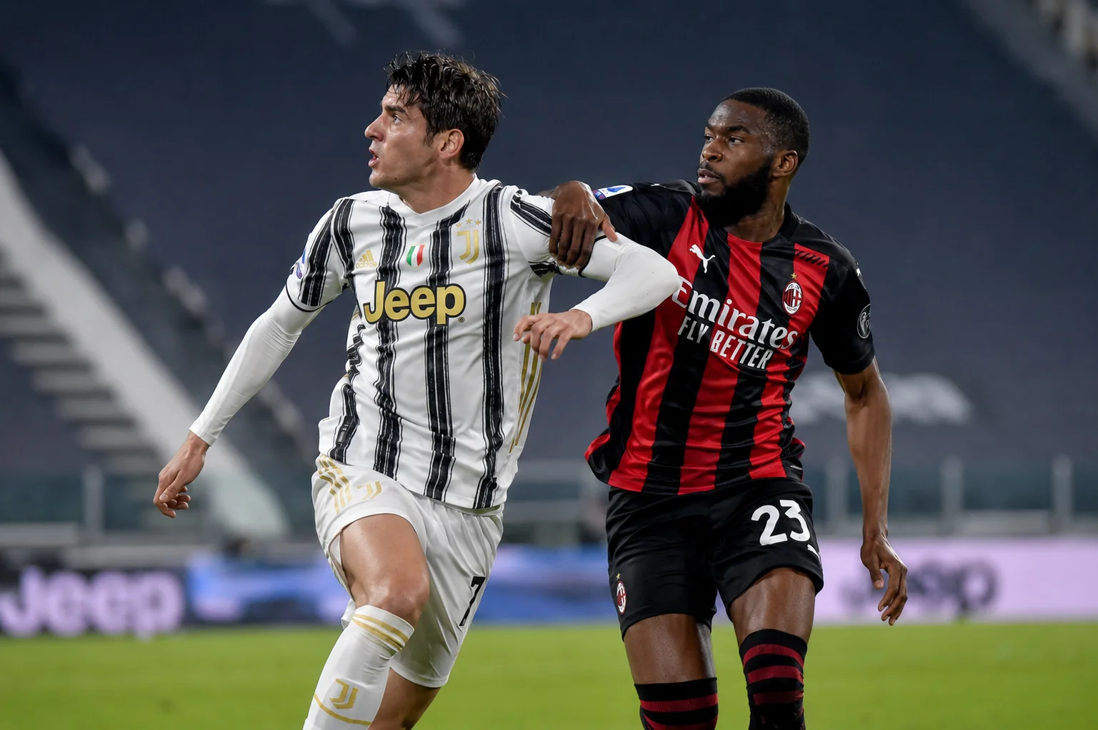 An action shot during a match showing Juventus defender Leonardo Bonucci shielding the ball in his team's iconic black-and-white vertical striped jersey featuring the "Jeep" sponsor logo. AC Milan defender Fikayo Tomori presses closely from behind in AC Milan's red-and-black kit, attempting to challenge for possession on the pitch.